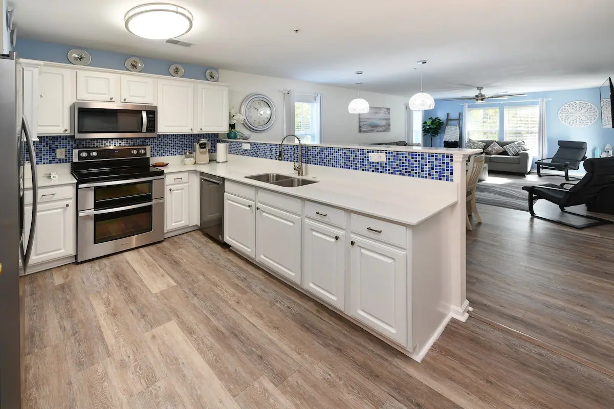 White kitchen peninsula with blue tile backsplash opening to living room