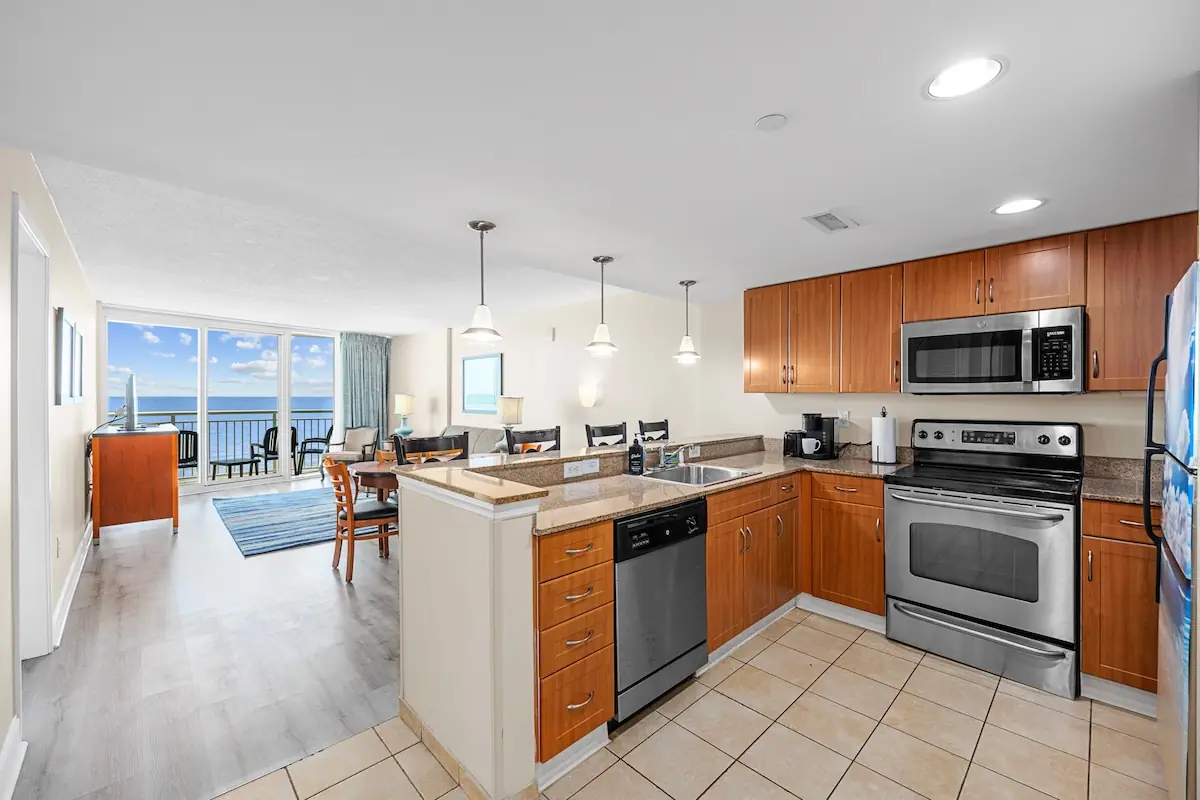 Wood-cabinet kitchen opening to a living area with ocean-facing glass doors