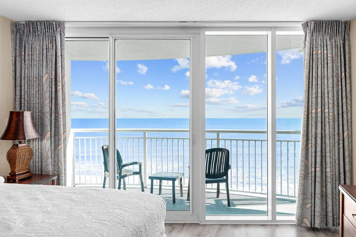 Bedroom glass doors opening to a balcony with chairs and ocean view