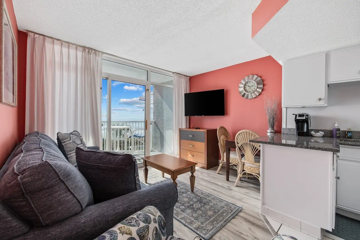Living room with a gray sofa, coral wall, kitchen, and balcony doors