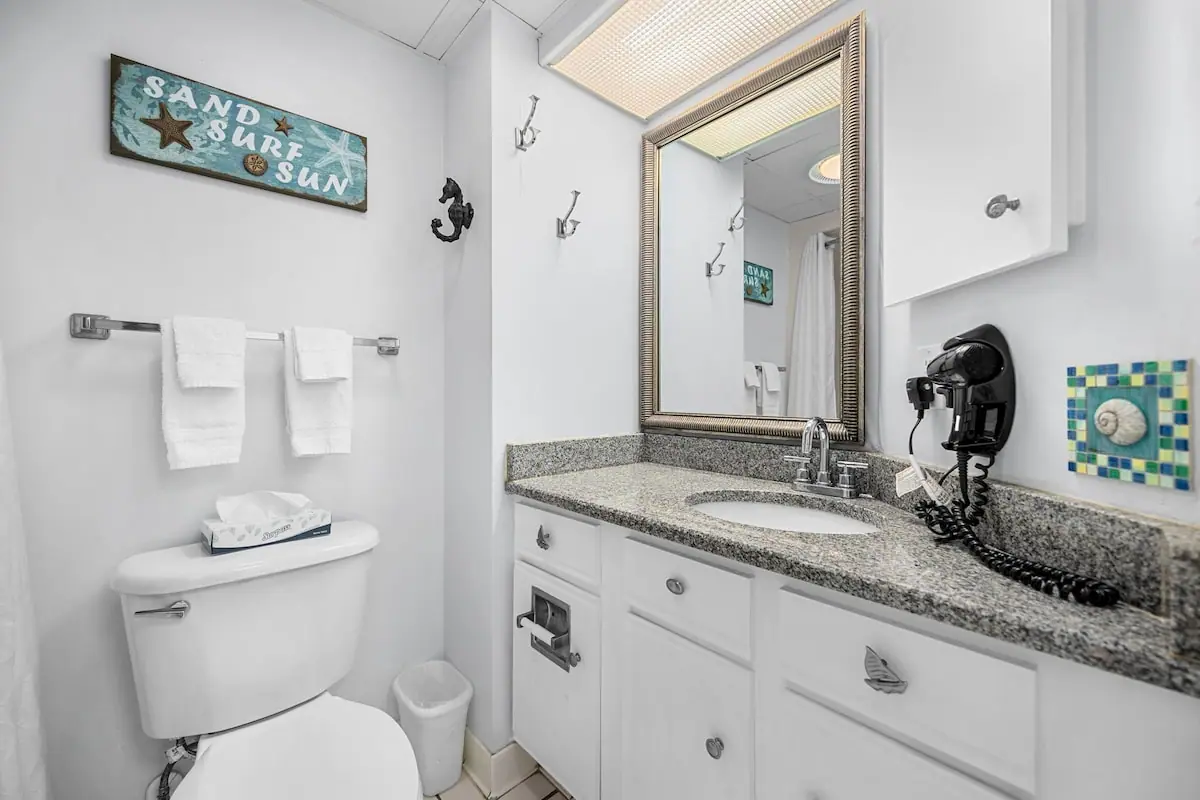 White bathroom with a granite-look vanity, framed mirror, and toilet