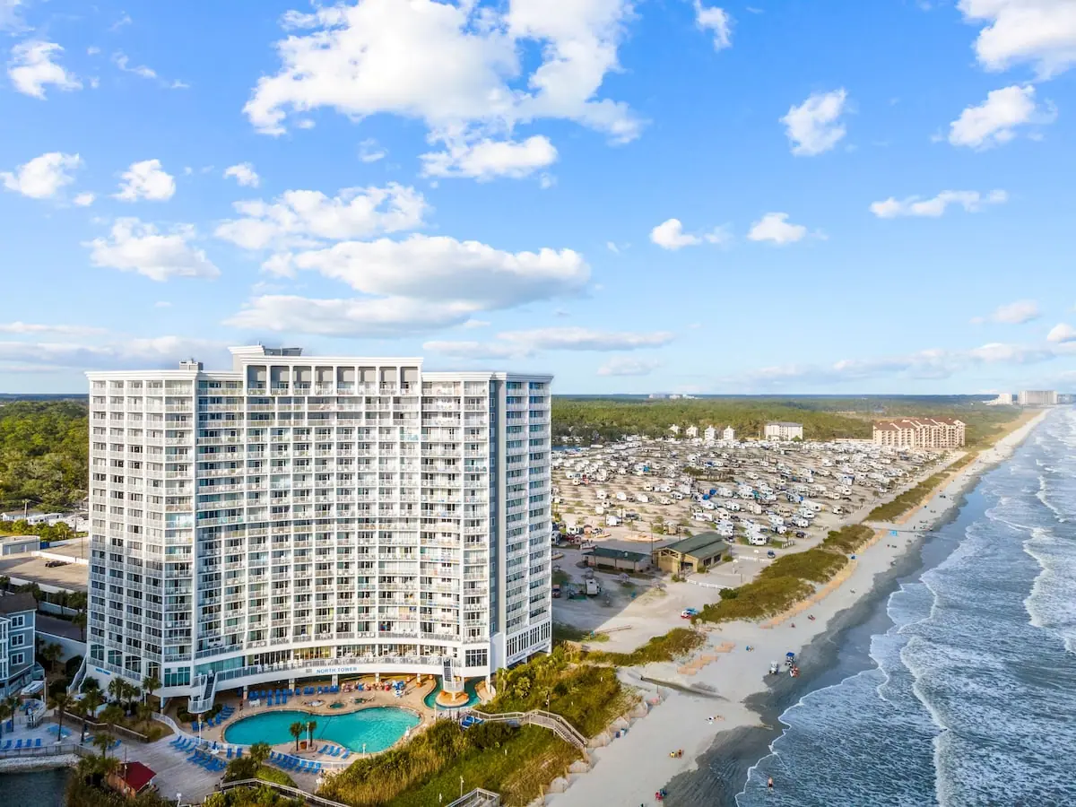 Aerial view of a beachfront building, outdoor pool, sandy shore, and ocean