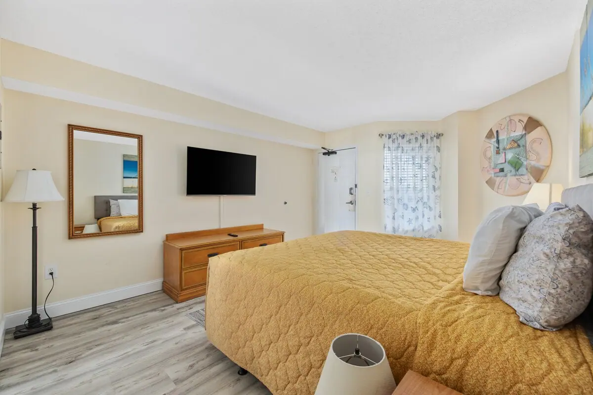 Bedroom with a yellow quilted bedspread, wall-mounted television, and wooden dresser