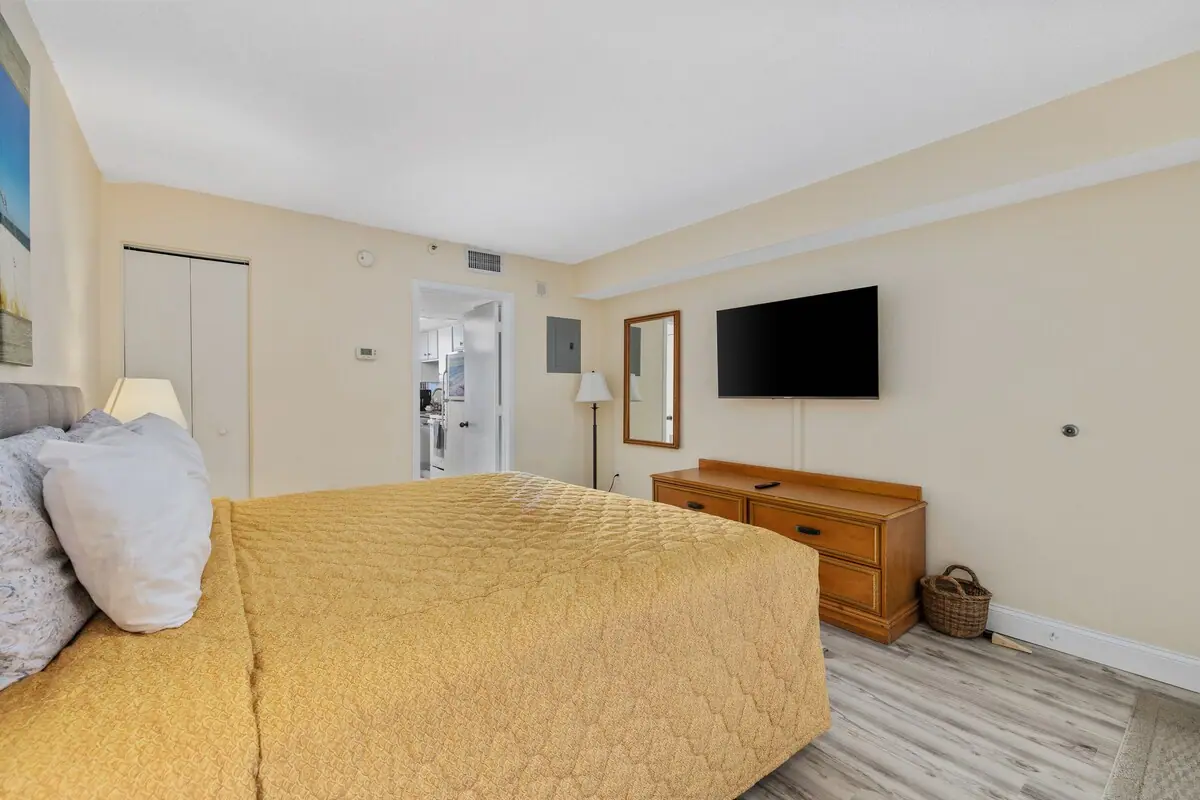 Bedroom with a yellow quilt and dresser beneath a wall-mounted television