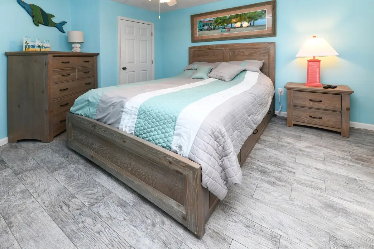 Bedroom with pale blue walls, a wooden bed frame, and dresser