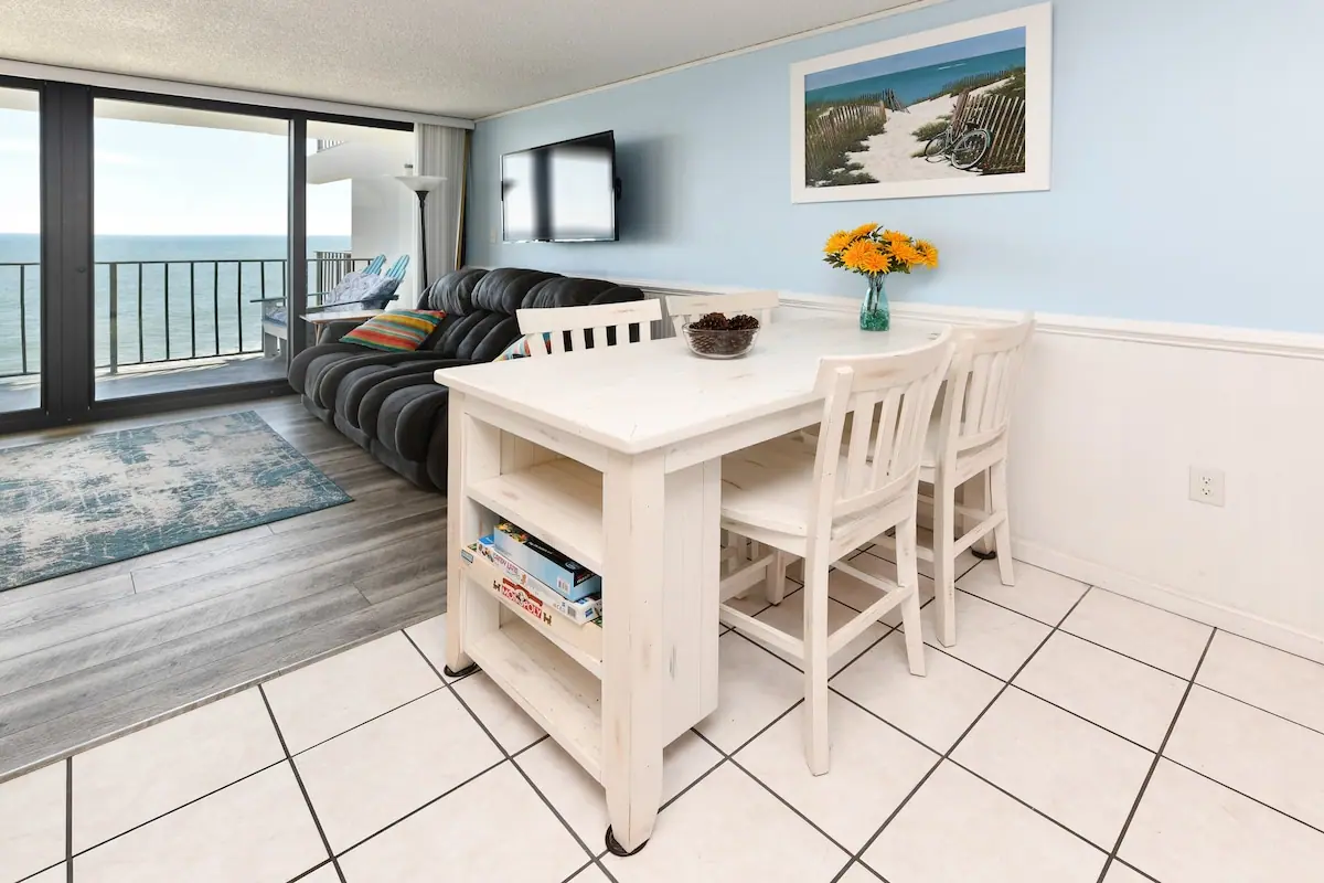 White dining table beside a living room and ocean balcony