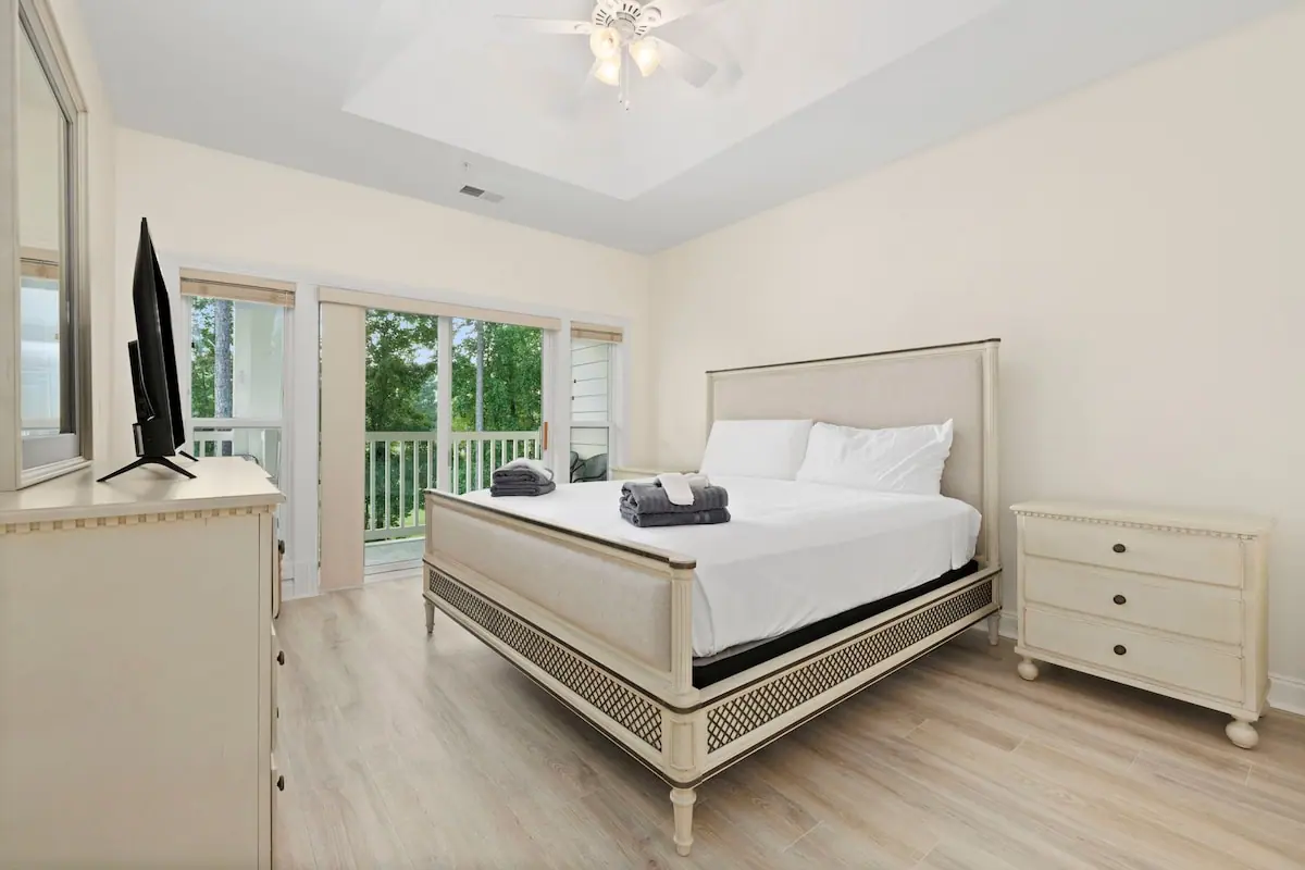 White bedroom with large bed, television, and glass patio doors