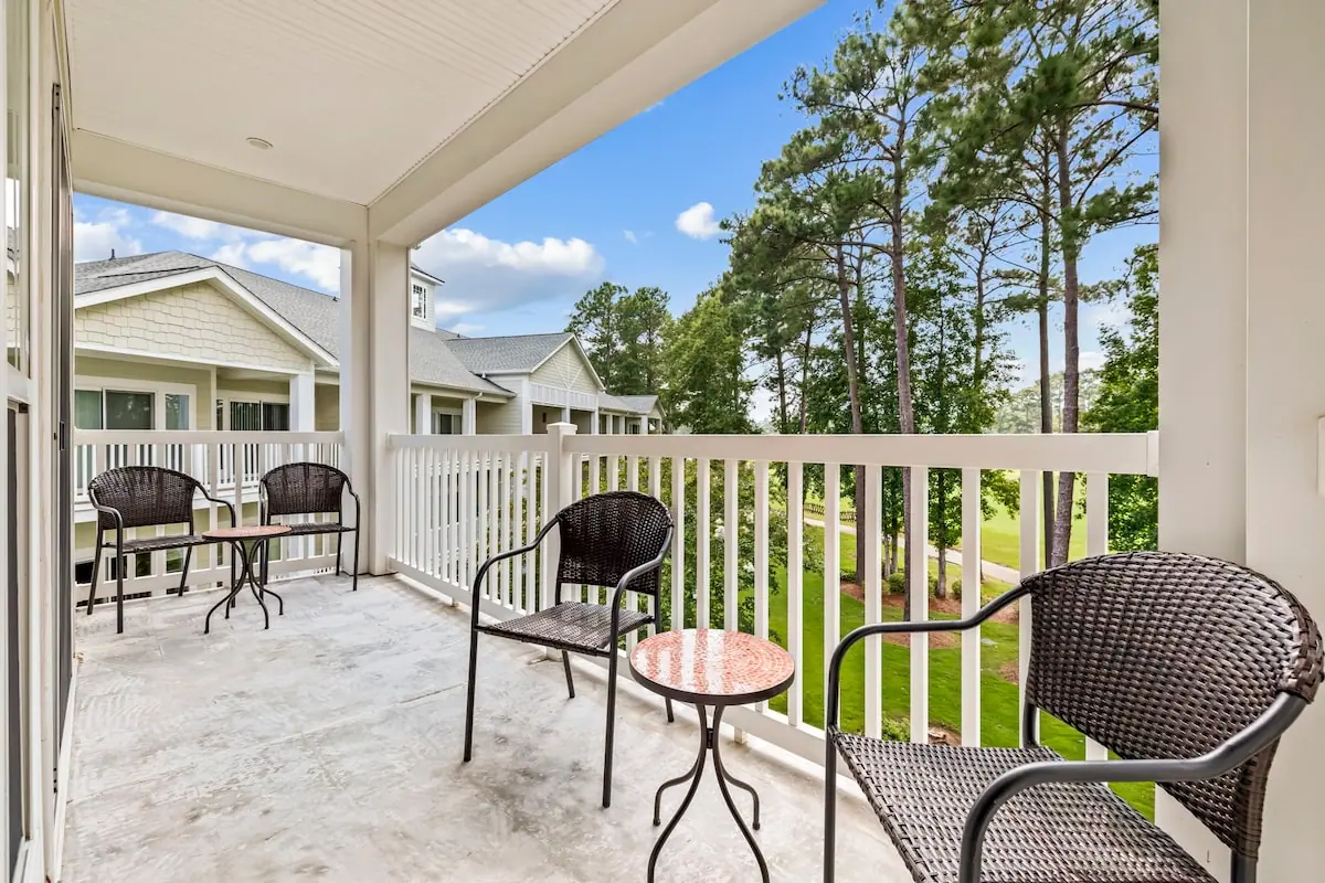 Covered balcony with wicker chairs facing trees and lawn