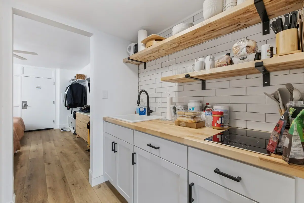 Compact kitchen with white tile backsplash, wooden shelves, and cooktop