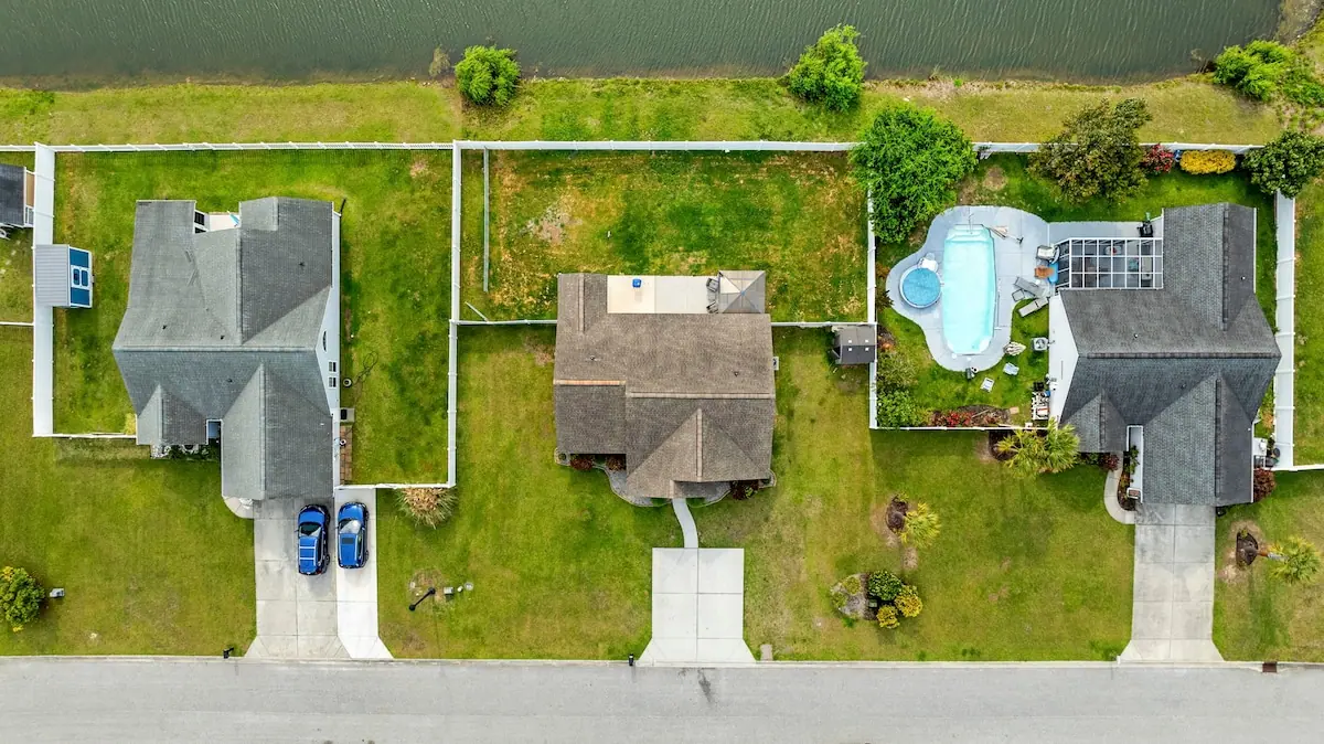 Overhead view of three fenced homes along a street, with a pool beside one of them