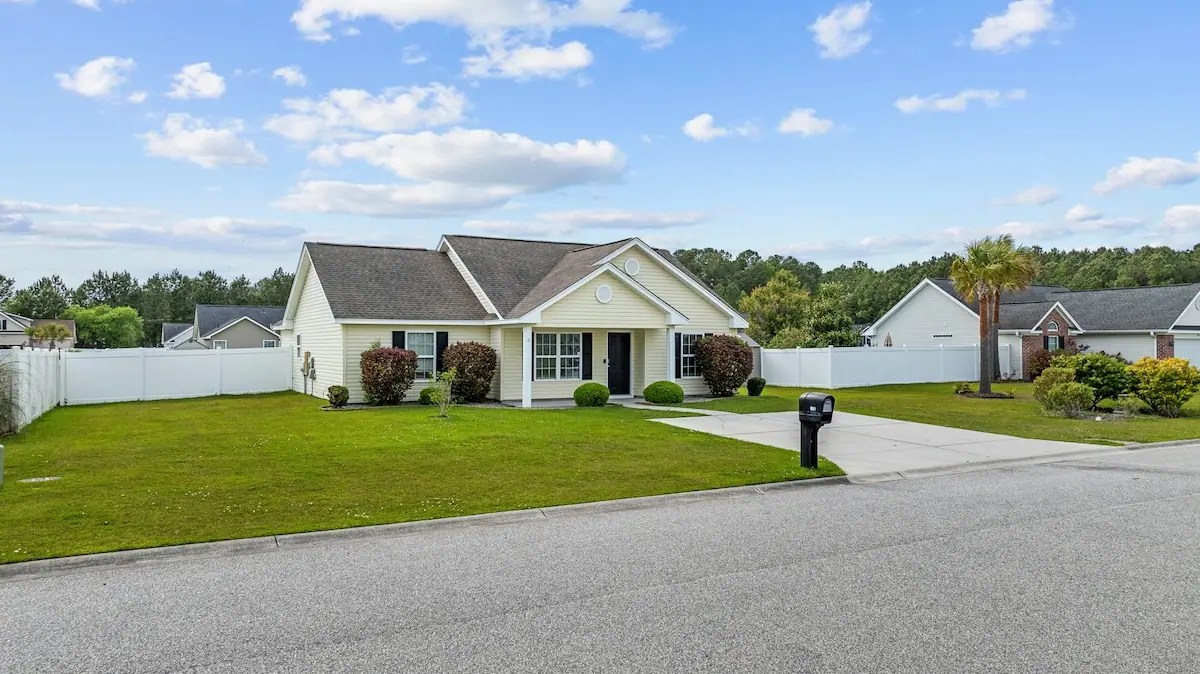 Pale yellow single-story home with lawn and white fenced yard