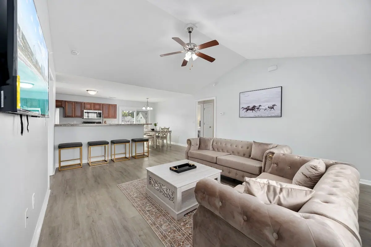Living room with plush gray sofas, television, and kitchen bar beyond