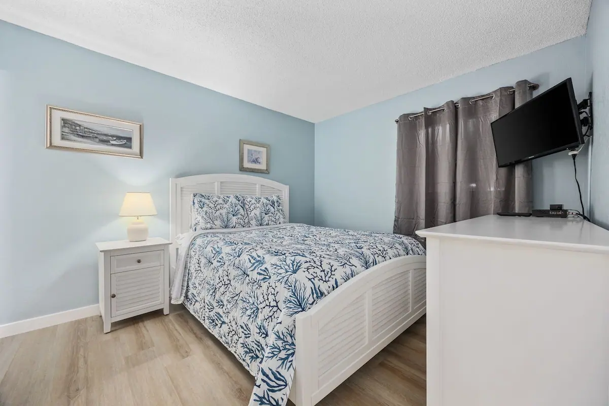 Bedroom with a white bed, blue and white patterned bedding, and TV