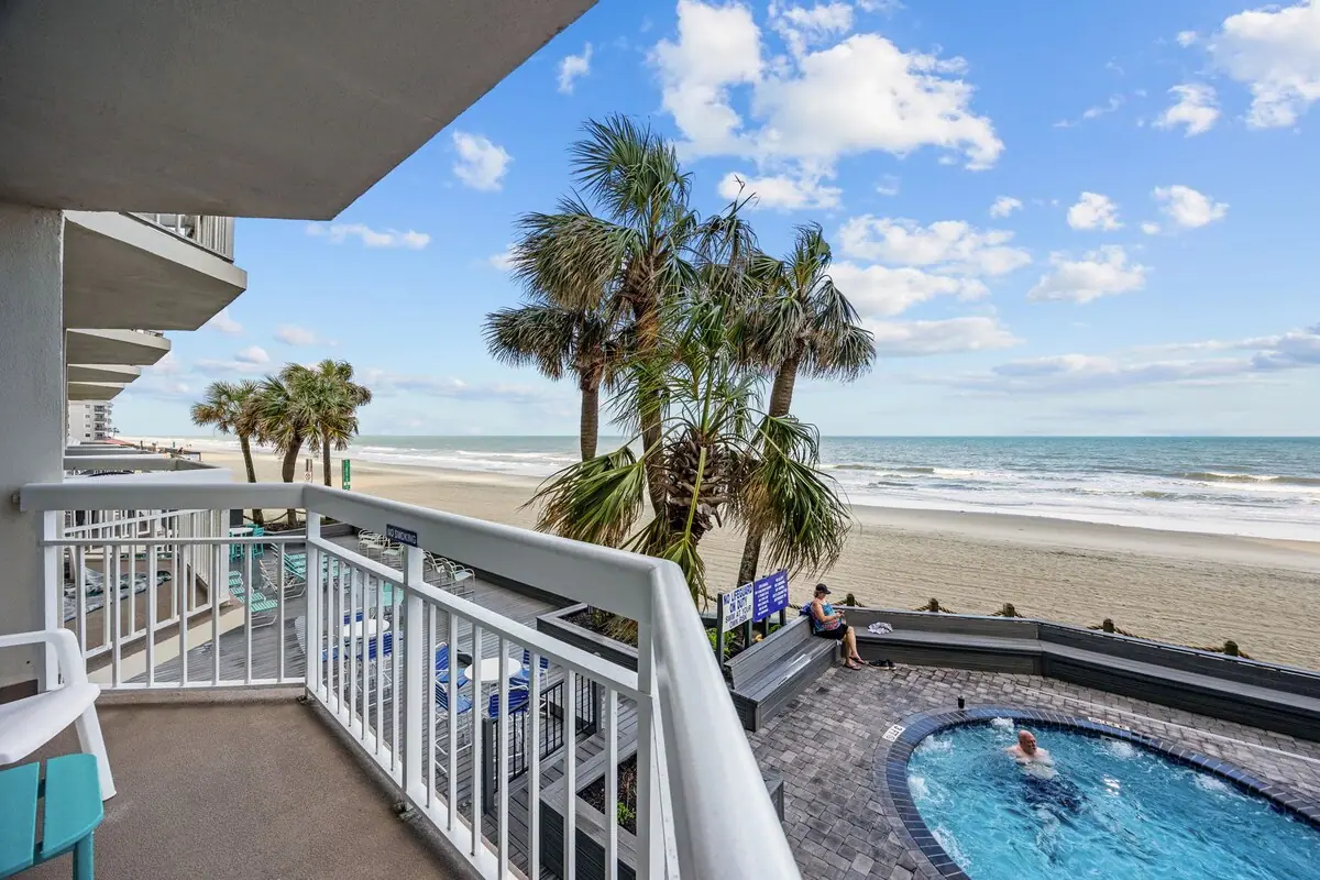 Covered balcony overlooking palm trees, pool, beach, and ocean