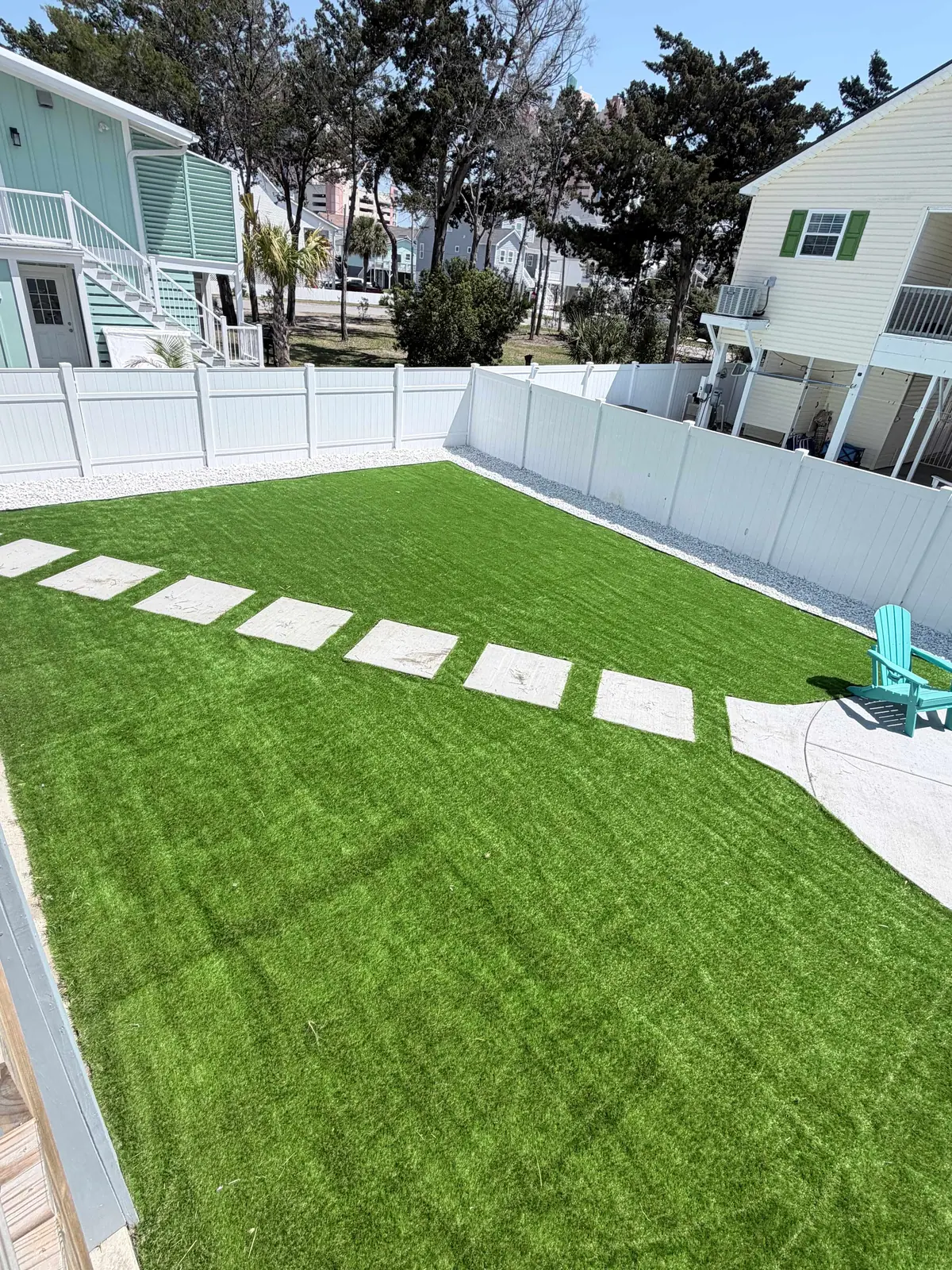 Fenced green lawn with stepping stones beside neighboring houses