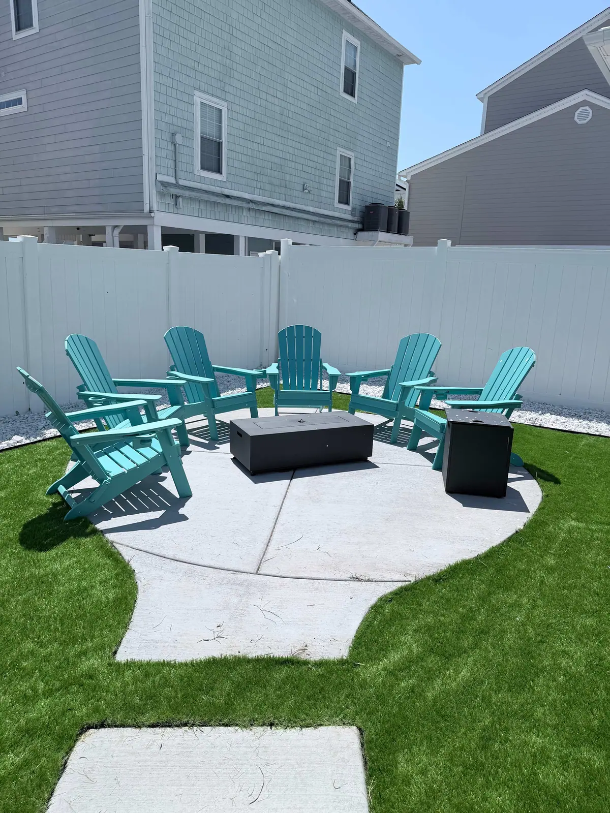 Turquoise outdoor chairs around a square fire pit in a fenced yard