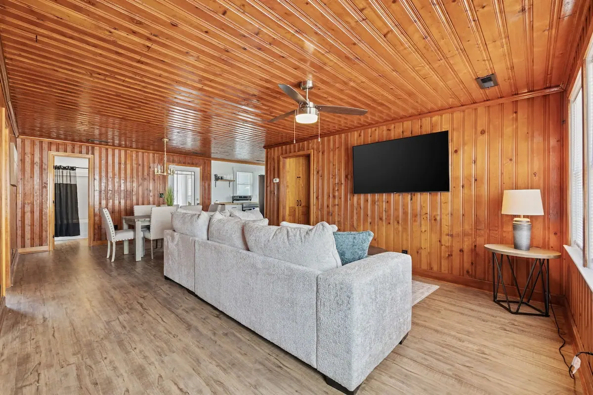 Living room with a pale sofa, wood-paneled ceiling, and wall-mounted television
