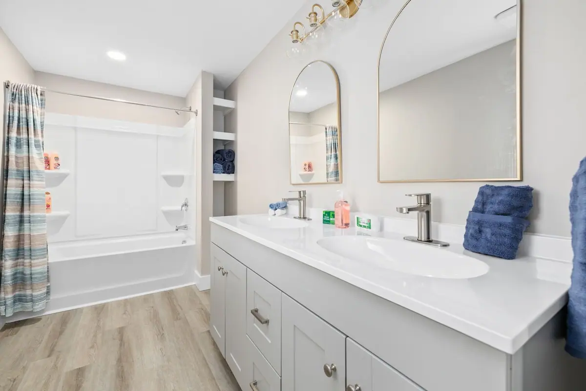 Bathroom with double white sinks, arched mirrors, and a tub-shower