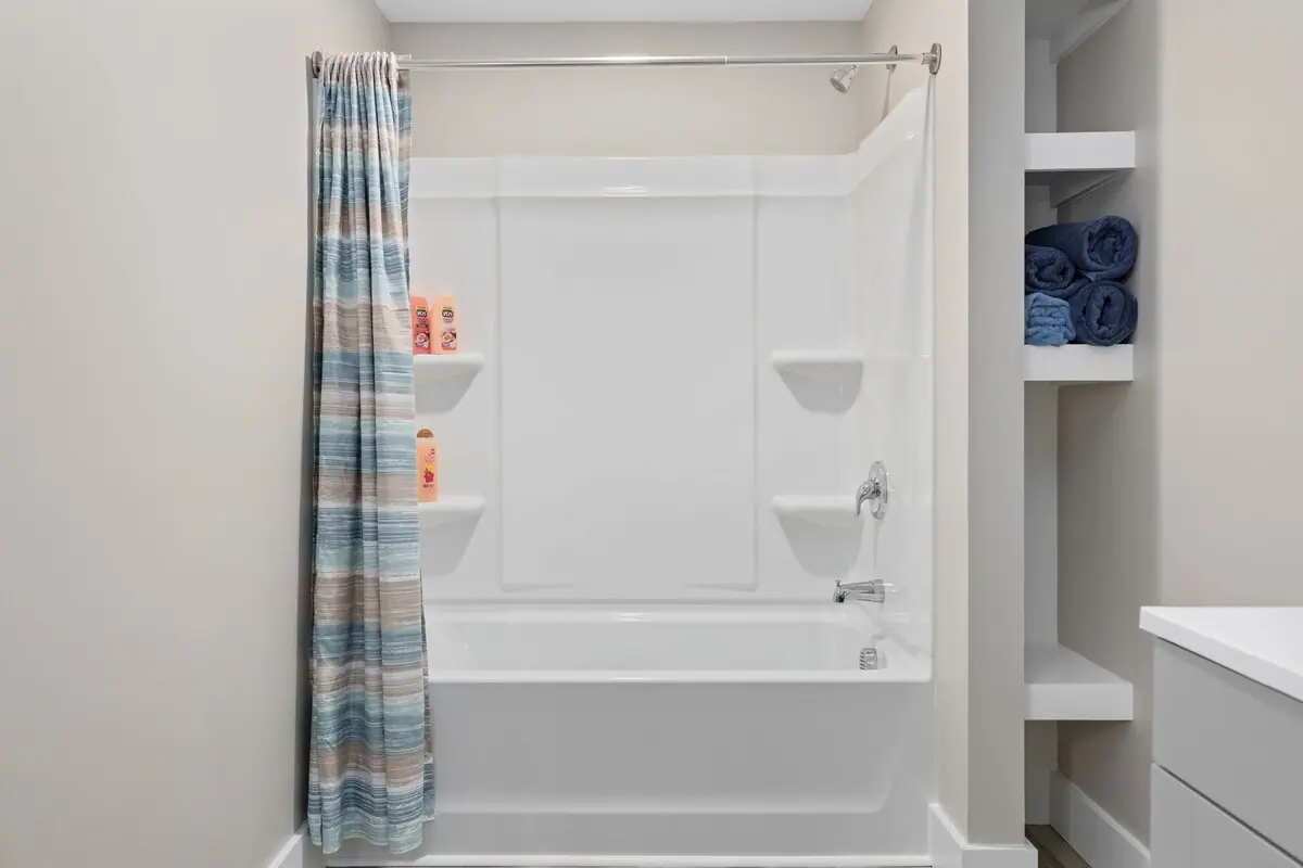 Tub-shower with patterned curtain beside shelves of folded blue towels