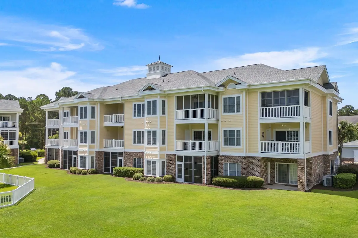 Exterior of yellow and white condo building across a green lawn