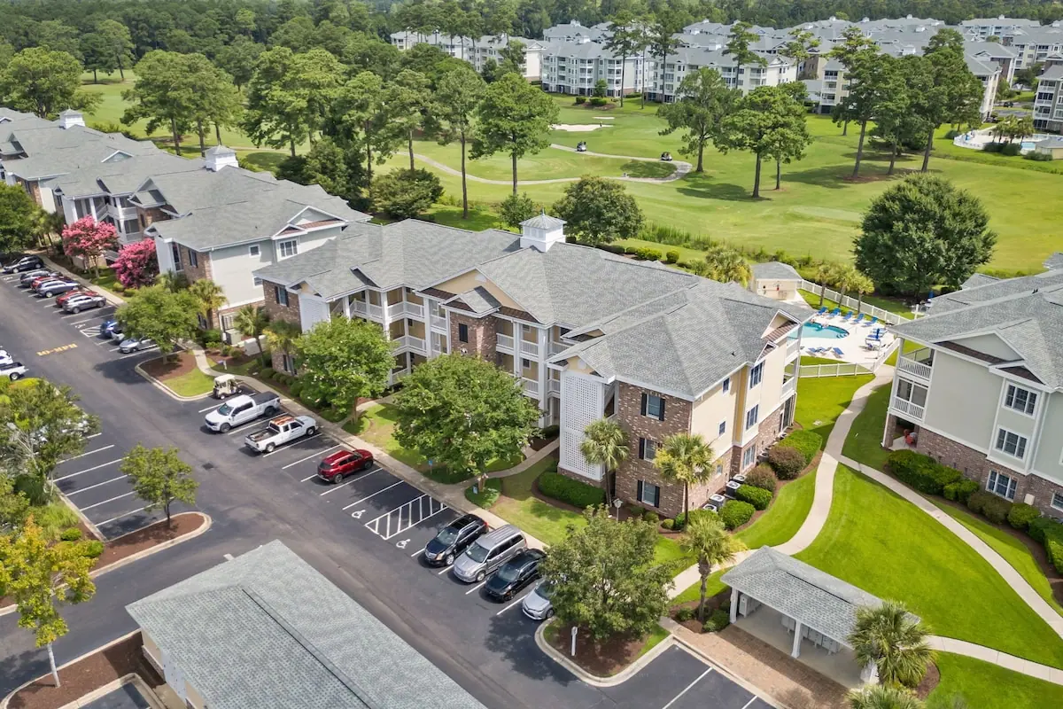 Aerial view of condo buildings, parking, and adjacent fairway