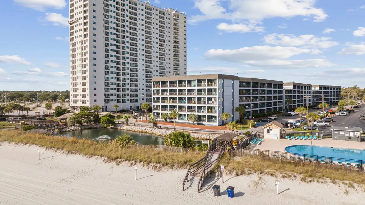 Resort buildings beside a sandy dune, with a boardwalk and outdoor pool in view