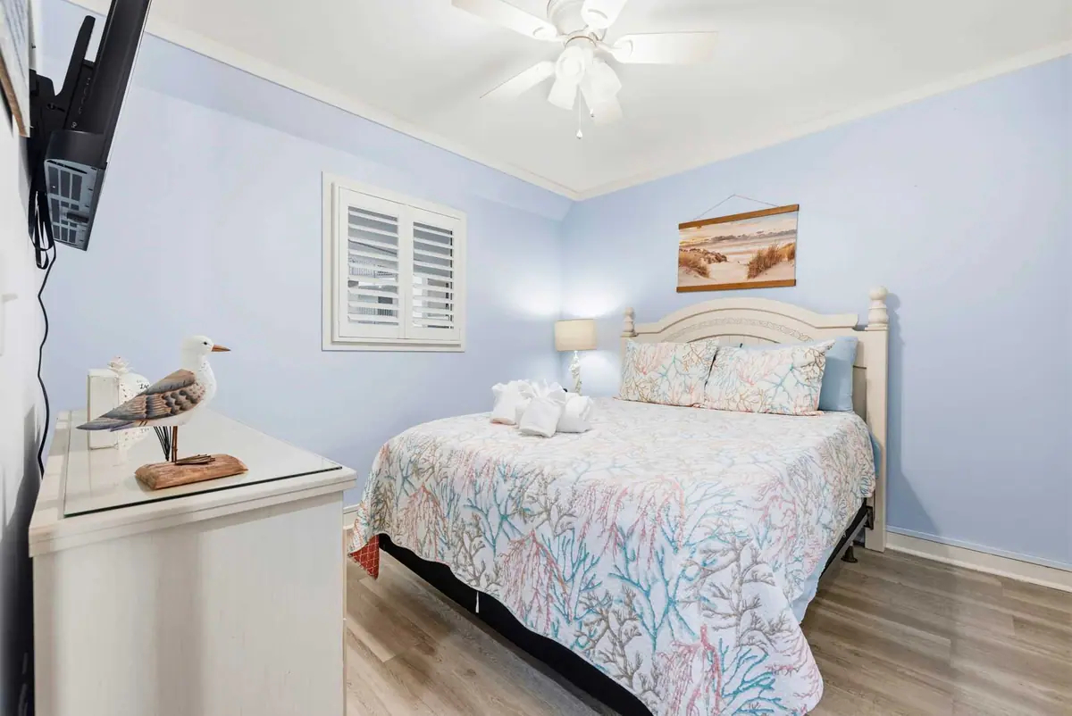 Bedroom with a white bed frame, patterned quilt, and pale blue walls