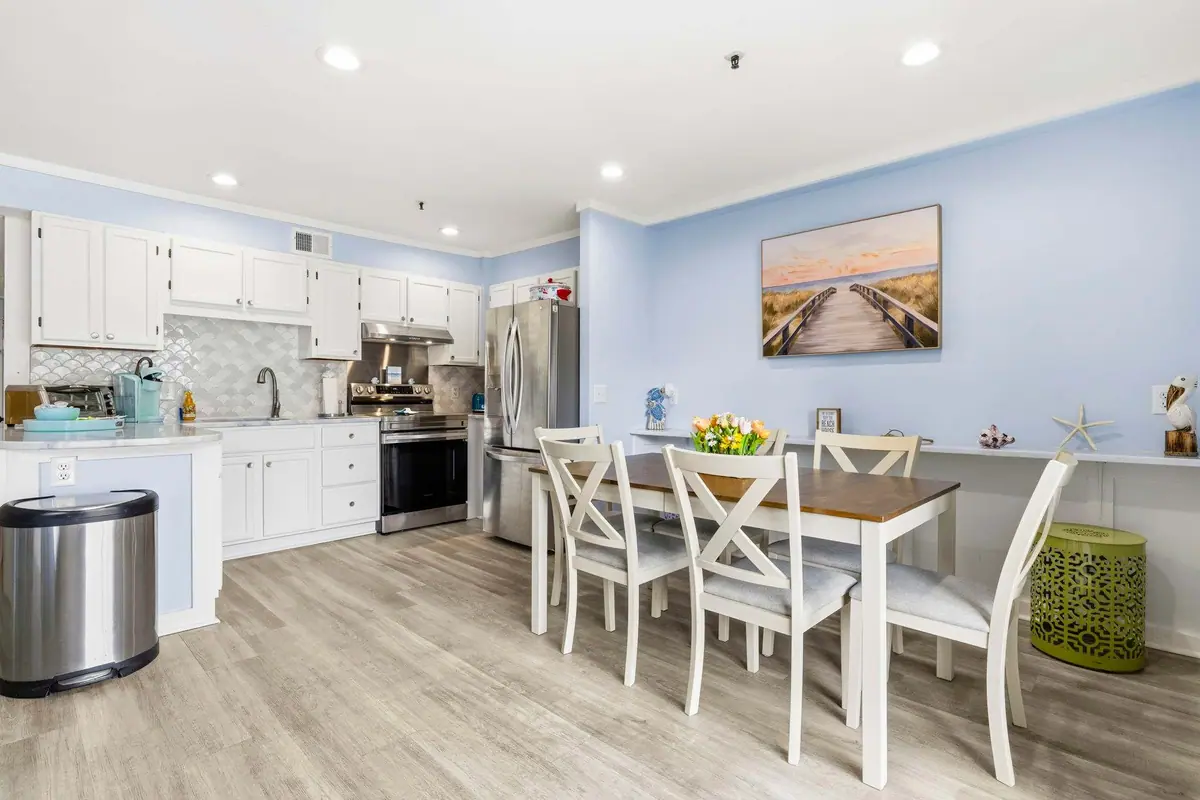 White kitchen and four-seat dining table beneath beach walkway artwork