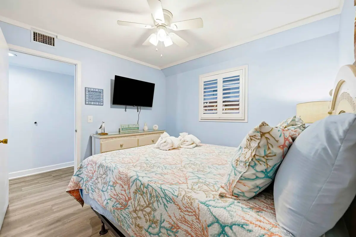 Bedroom with patterned bedding, wall-mounted television, and shuttered window